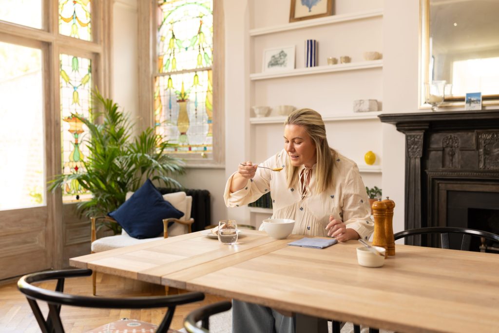 Woman eating soup sat at kitchen table